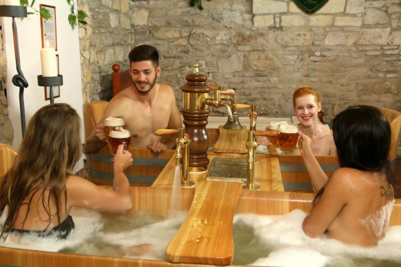 Lidé relaxují v dřevěné vaně s pivem.
