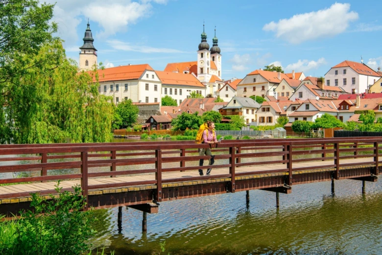 Turista kráčí po mostě v Telči s historickým městem na pozadí.