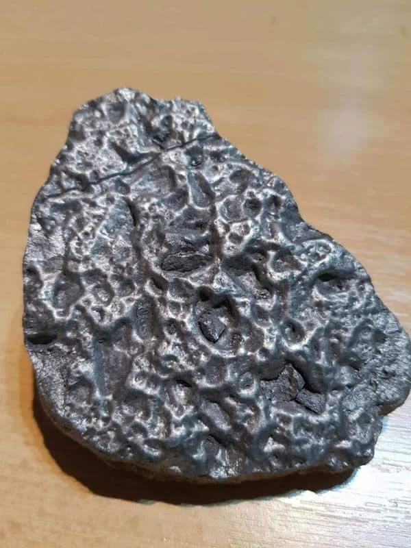 Meteorit s typickou povrchem v podobě kráterů na dřevěném podkladu.