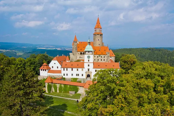Bouzov hrad na kopci obklopený zelenou přírodou.