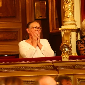 Žena v zlatém balkóně divadla aplauduje.