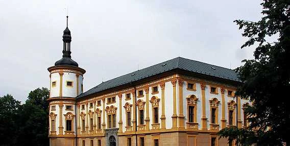 Historická budova v Krnově s věží na pozadí stromů.