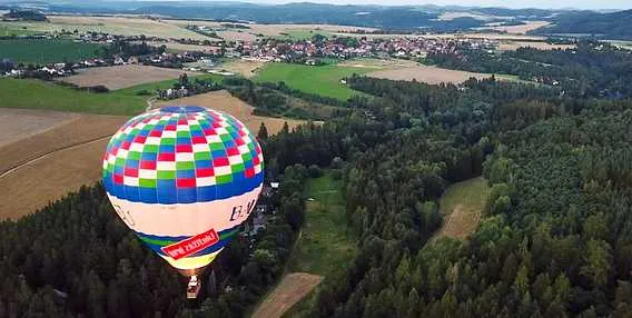 Barevný vzducholod nad českou krajinou s lesy a vesnicemi.