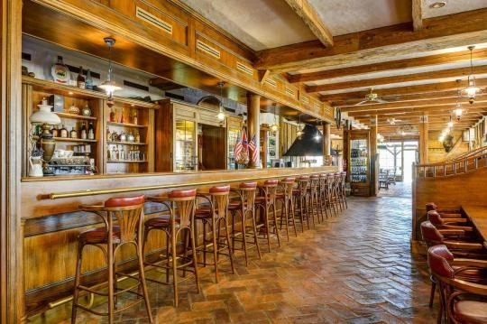 Vnitřek restaurace s dlouhým dřevěným barem a červenými židlemi.