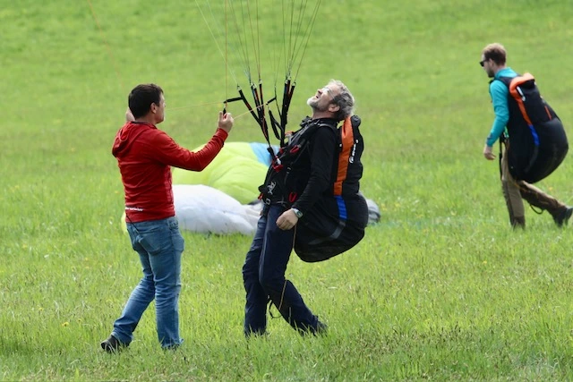 Tři lidé připravují parašutistické vybavení na trávníku.