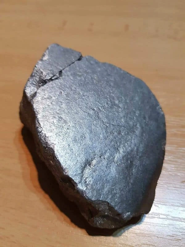 Tmavý kousek meteoritu s kovovým leskem na dřevěném povrchu.