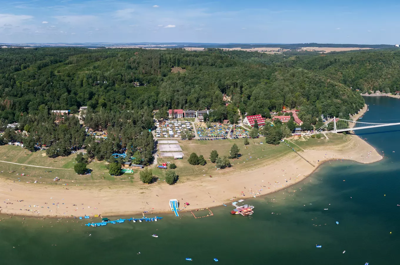 Pohled na české jezero s pláží, hotely a rekreačními zařízeními.