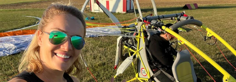 Žena s brýlemi stojí vedle žlutého parašutistického vybavení na trávníku.