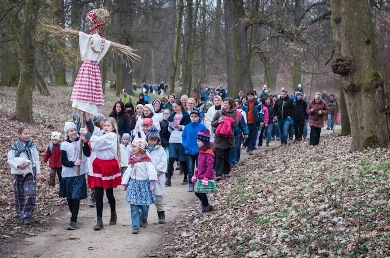 Děti nesou masopustní kuklu v lese při průvodu.