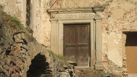 Historický kamenný portál s dřevěnými dveřmi v ruinách tvrze.