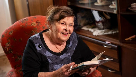 Starší žena sedí v křesle s otevřenou knihou.