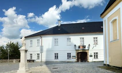 Historická bílá budova s dvorem v Mohlnici pod modrou oblohou.
