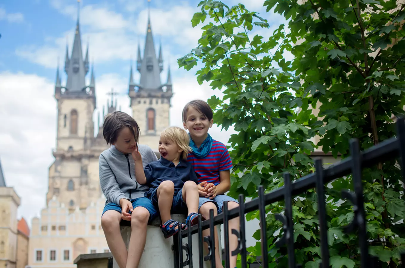 Three boys sitting on a fence with prague's old town bridge