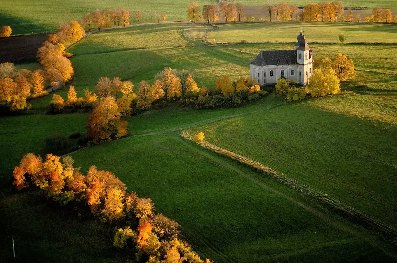 Kostel v podzimní krajině s žlutými listy.