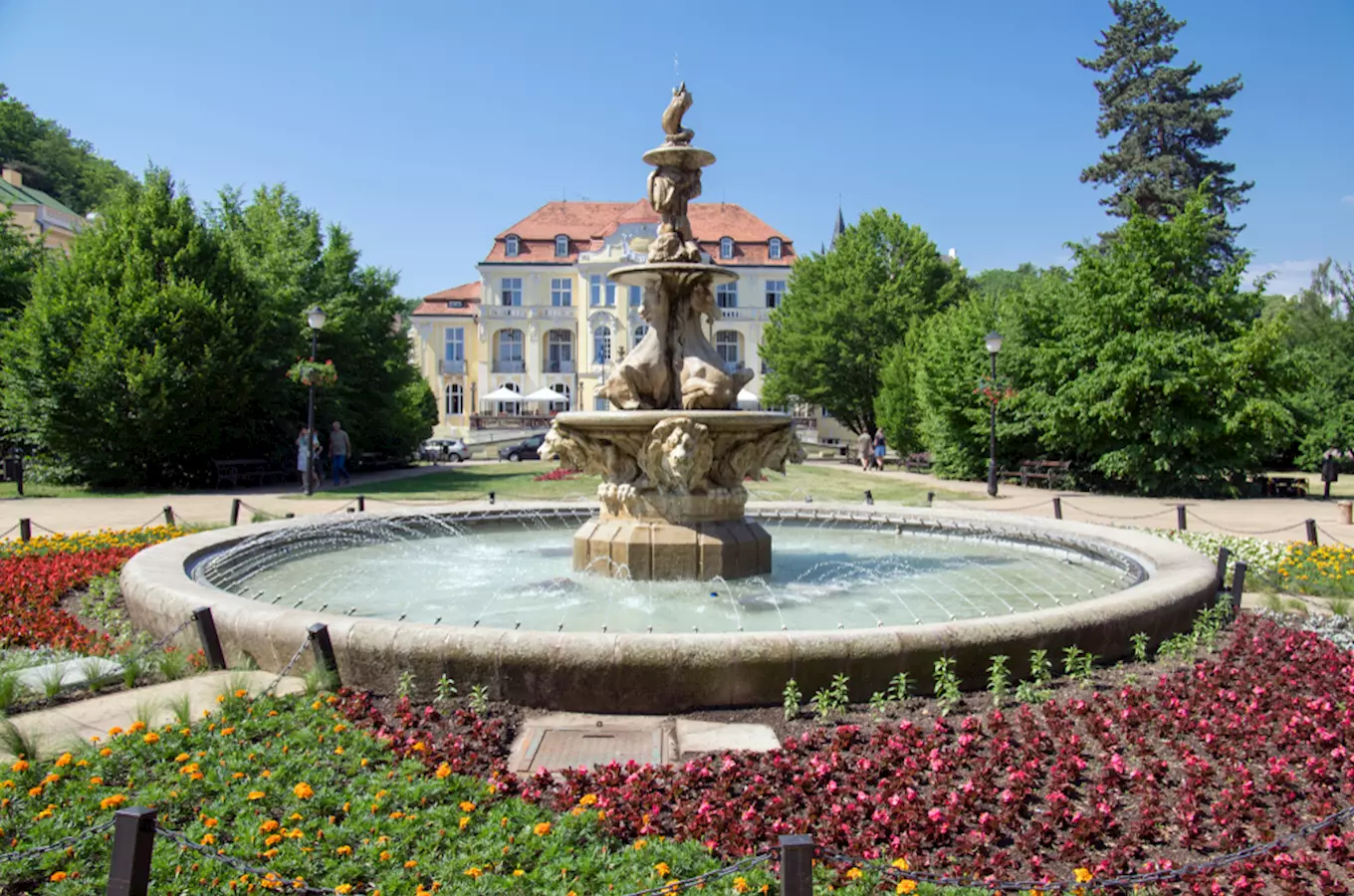 Fontána v parku s květinami před historickým domem.