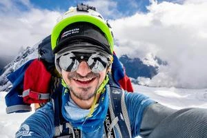 Smějící se horolezec dělá selfie na sněhové hoře.