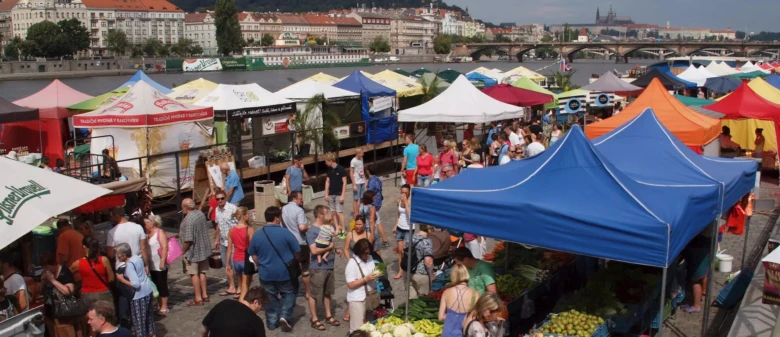 Venkovní trh s barevnými stany na břehu řeky v Praze.