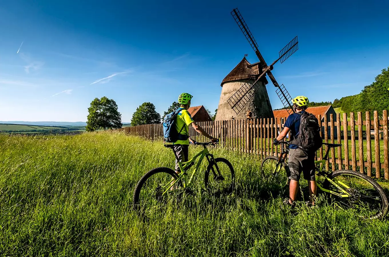 Dva cyklisté u starého větrného mlýna na českém venkově.