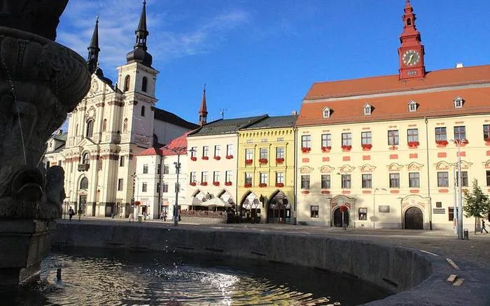 Fontána na náměstí v Jihlavě s kostelem a barevnými domy.