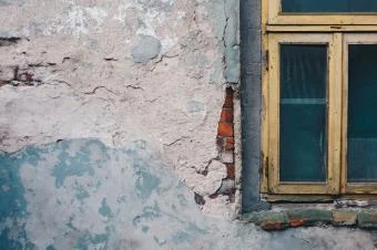 Zanedbaná fasáda domu s oknem na pozadí.