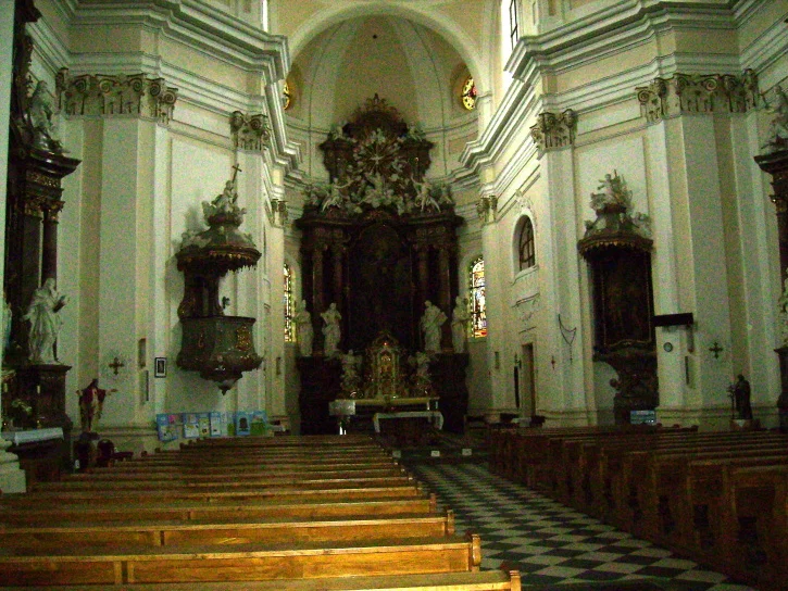 Vnitřek historického kostela s dřevěnými lavicemi a oltářem.