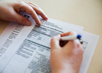 Ruce vyplňují formulář na papíře s modrým perem.