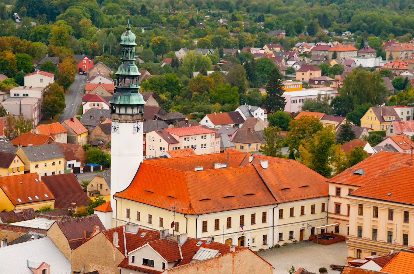 Domažlice náměstí s radnicí a věží na pozadí zelených kopů.