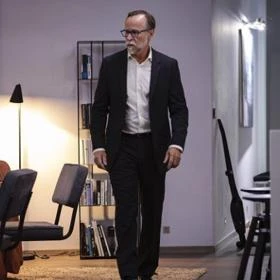 Herec Karel Roden v obleku kráčí po kancelářské místnosti.