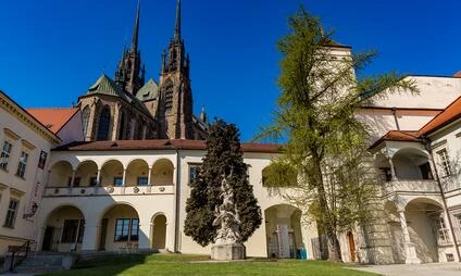 Kostel svatého Petra v Brně s arkádami a sochou na trávníku.