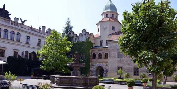 Historické hradní dvůr s fontánou a stromy v Rychnově nad Kněžnou.