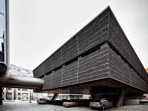 Brutalistní budova s tmavou fasádou v pražském městském prostředí.