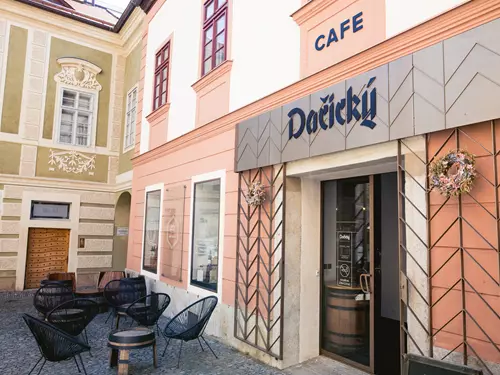Vstup do kavárny Dačický v historické ulici s venkovním posezením.