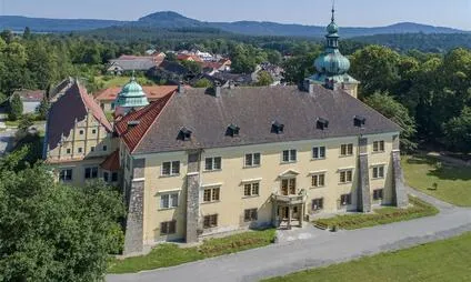 Zámek v Doksech s věžemi na pozadí zelených hor.