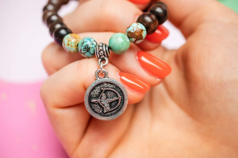 Rukou drží náramek s amuletem Střelce zvěrokruhu.