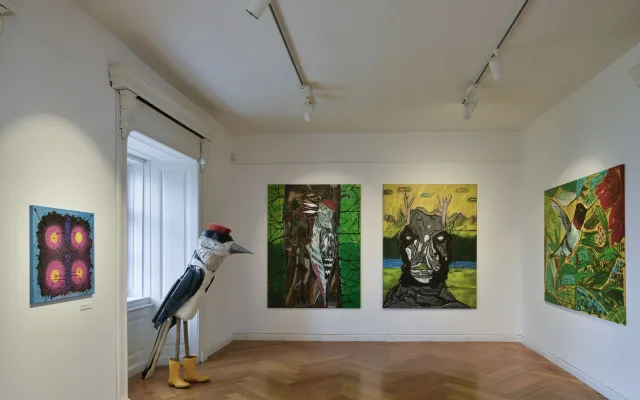 Výstava obrazů v galerii s sochou dravého ptáka.