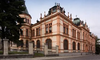 Historická budova v Klatovech s arkýřovými okny a ozdobnou střechou.