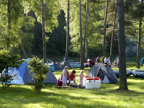 Rodina kempuje s dětmi v lese u stanu.