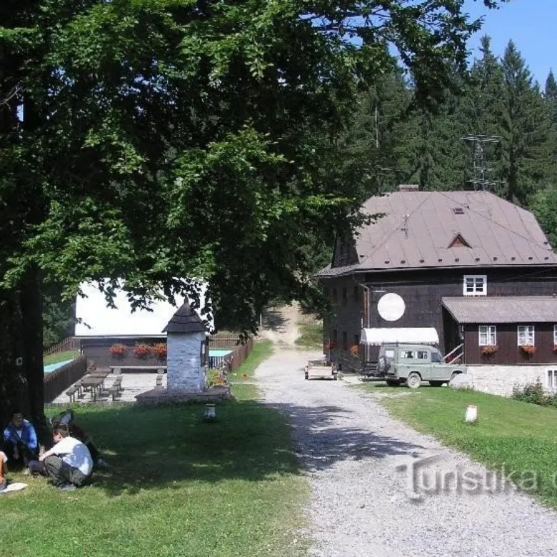Tradiční dřevěný dům v Bílých Beskydách s cestou vedoucí k lesu.
