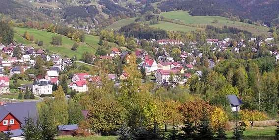 Pohled na obec Harrachov v horách s domy a lesy.