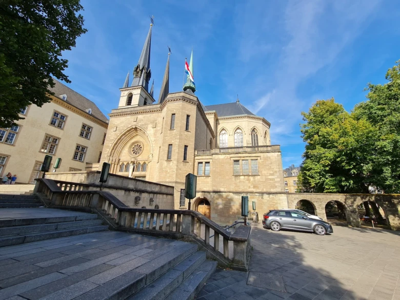 Katedrála v Lucemburku na slunečním náměstí s okolními stromy.