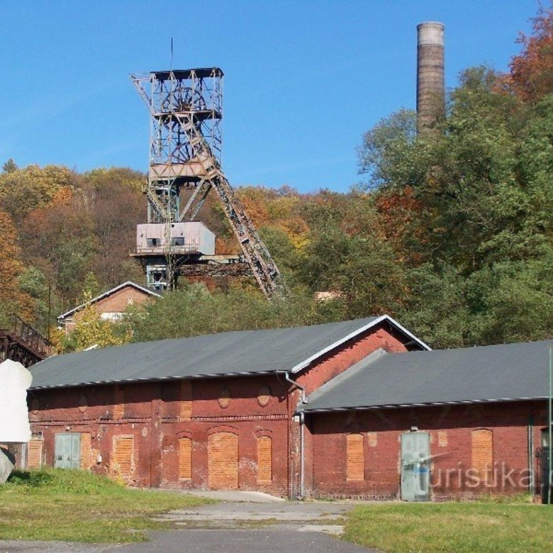 Historické průmyslové budovy s dolem v Ostravě na pozadí podzimního lesa.
