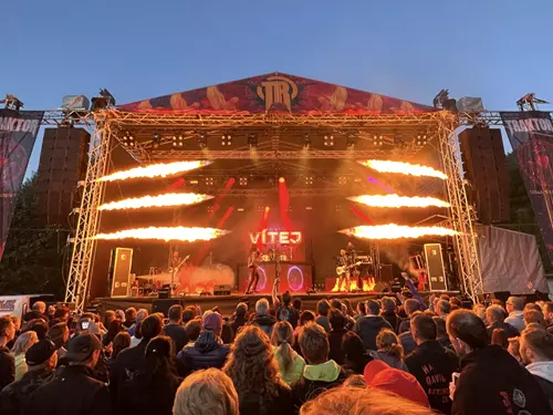 Koncert na venkovním pódiu s diváky za soumraku.
