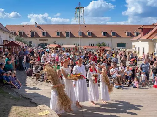 Ženy v bílých šatech tančí s svazky slámy na venkovském festivalu.