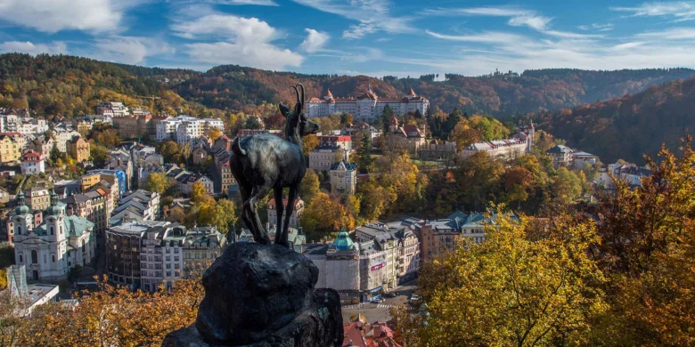 Bronzová socha kozla s výhledem na město Karlovy Vary.