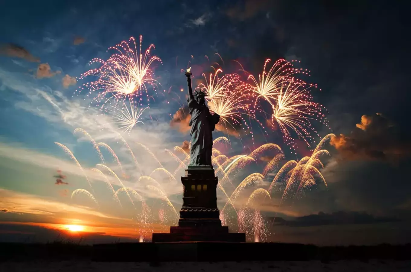 Statue of Liberty s oslavou ohňostrojem na pozadí západu slunce.