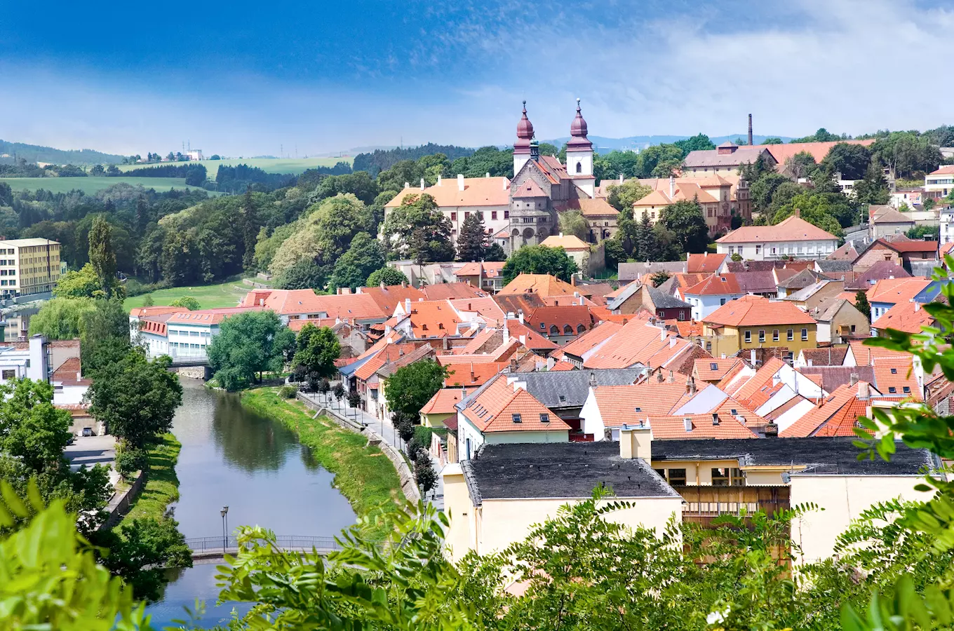 Pohled na město Třebíč s řekou, kostelem a červenými střechami.