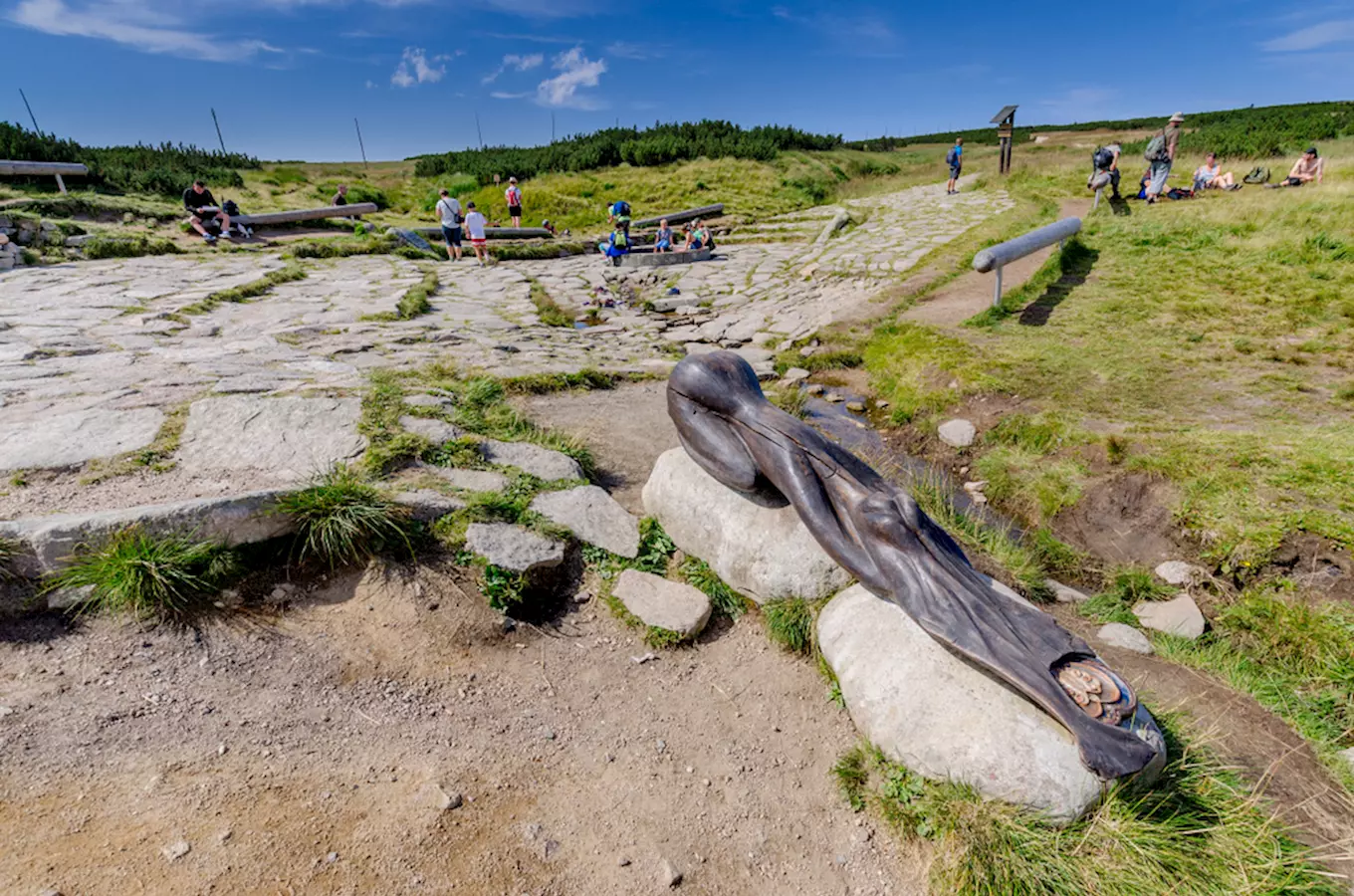 Socha u pramene řeky Labe s kamenitou cestou a turisty.