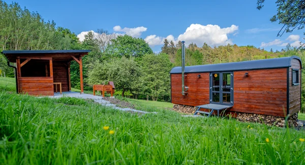 Dva dřevěné ubytovací chatky pro glamping na travnatém svahu.