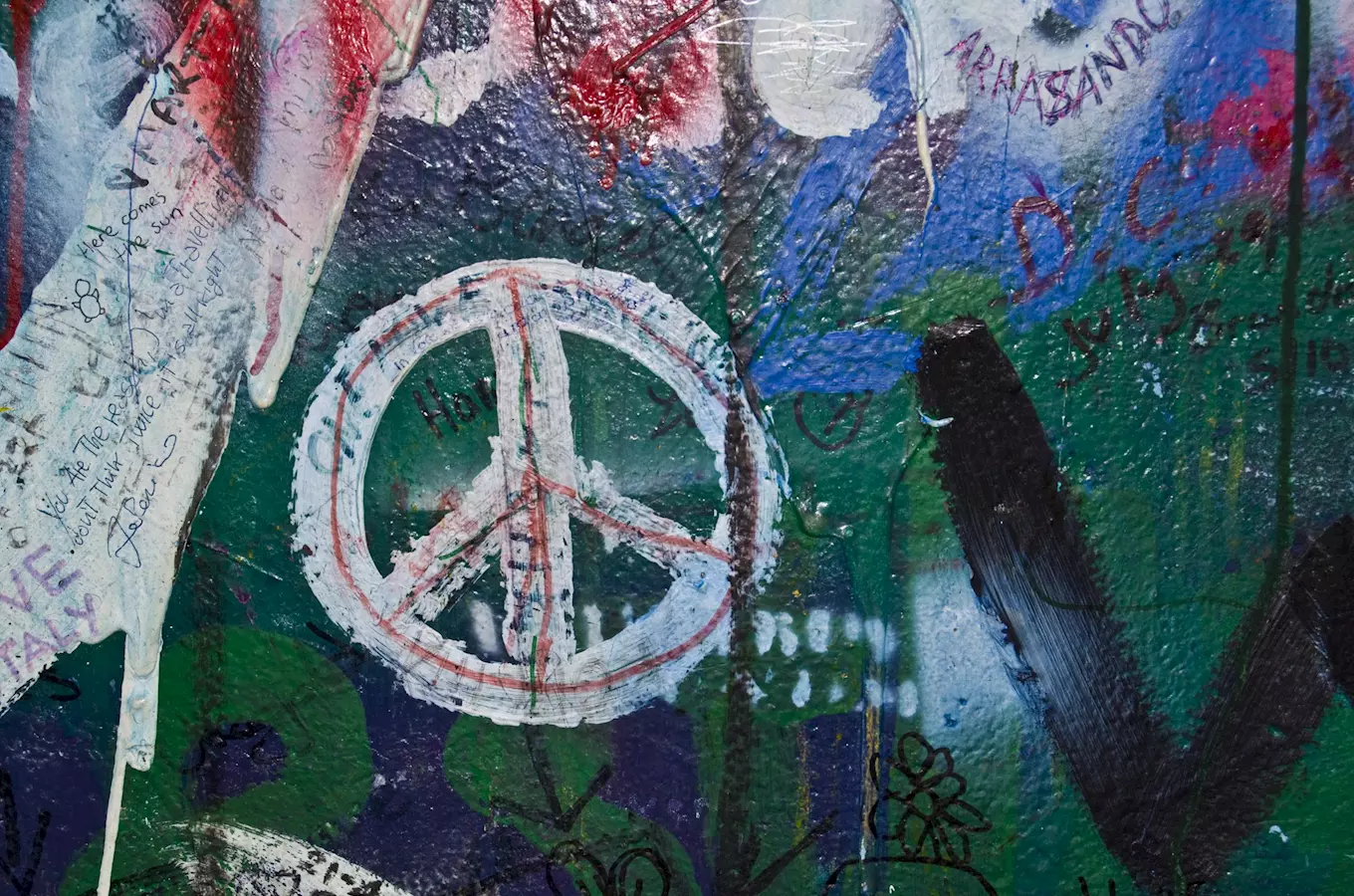 Bílý symbol míru na zdi s grafitovými nápisy v Praze.