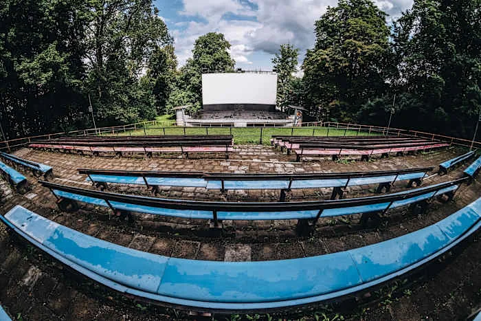 Prázdná letní kino s modrými lavicemi před velkým bílým plátnem.